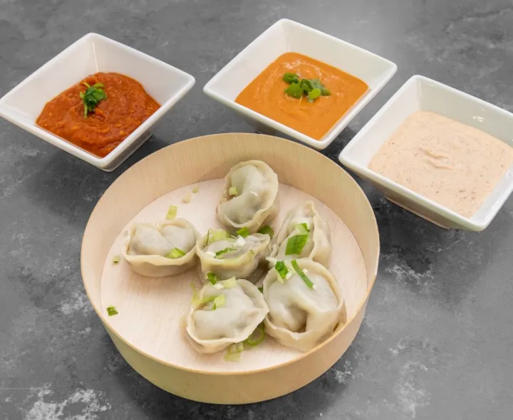 Steamed momo in a wooden bowl with three dipping sauces